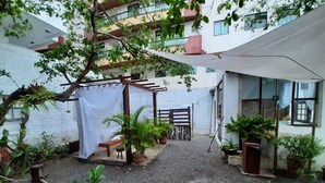 Un patio exterior con una pérgola, plantas en macetas, un banco y un edificio con ventanas.
