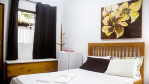 Un dormitorio con una cama, un refrigerador blanco pequeño, una ventana con cortinas y un cuadro de flores en la pared.