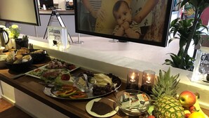 A buffet table with various food items and a television screen displaying a baby.