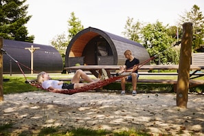 Two people relaxing on a hammock between two cabins with a wooden bench in the foreground.