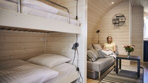 A bunk bed with a desk and a couch in a cabin-style room with wooden walls and a curved ceiling.