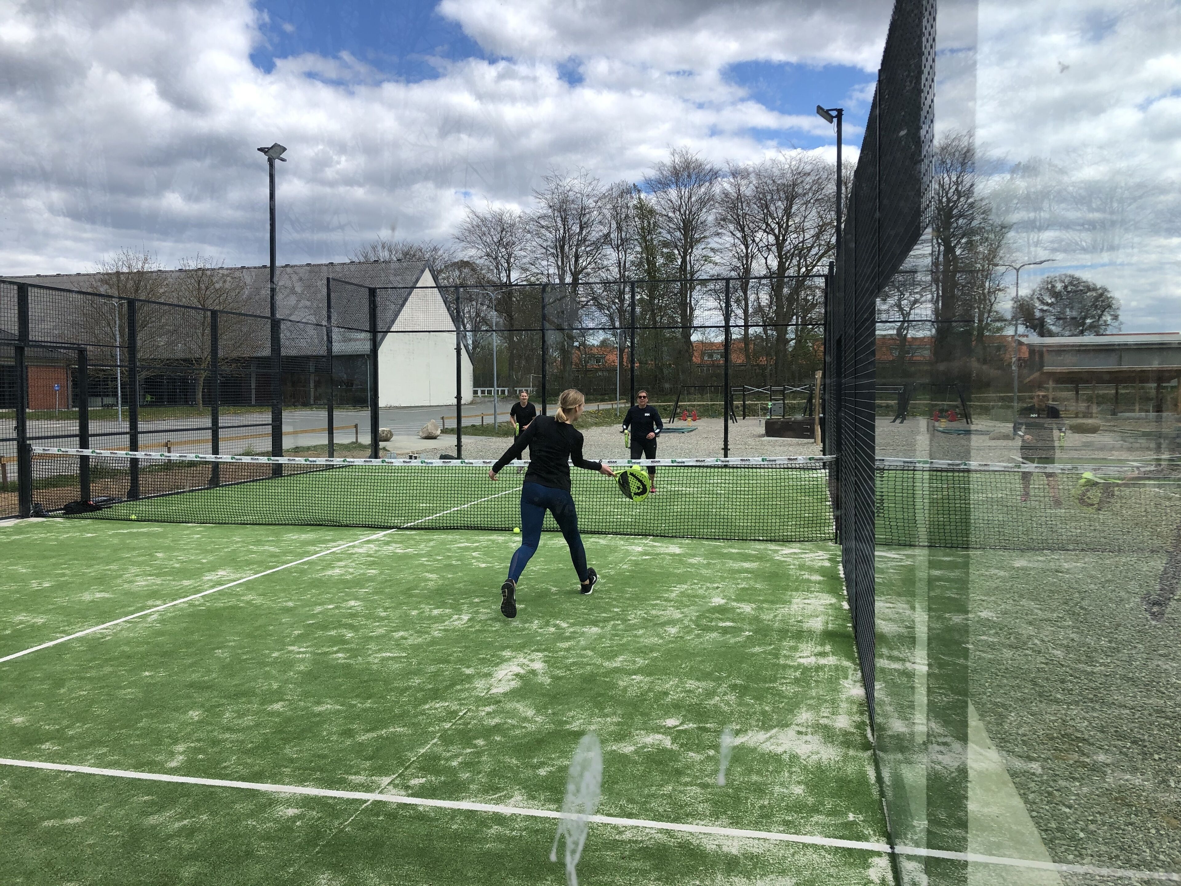 An indoor tennis court with a net, a fence, and a building in the background.