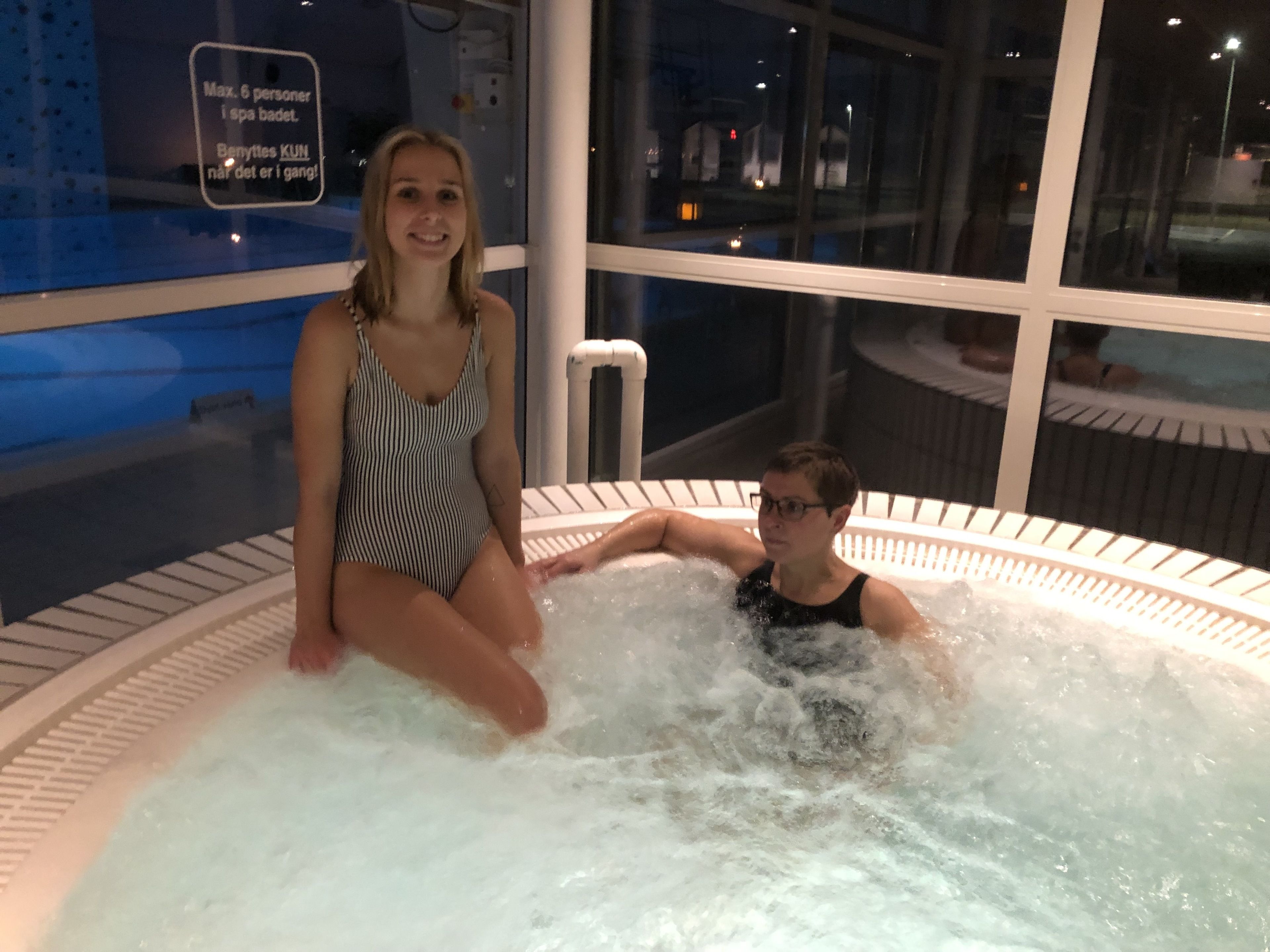 A couple in a hot tub with a view of a swimming pool and a sign indicating a maximum of 6 people in the spa area.