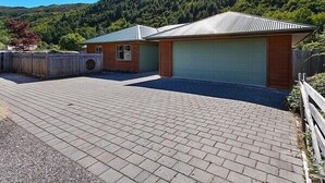 Een tweelaags huis met een garage, een verharde oprit en een glooiend landschap op de achtergrond.