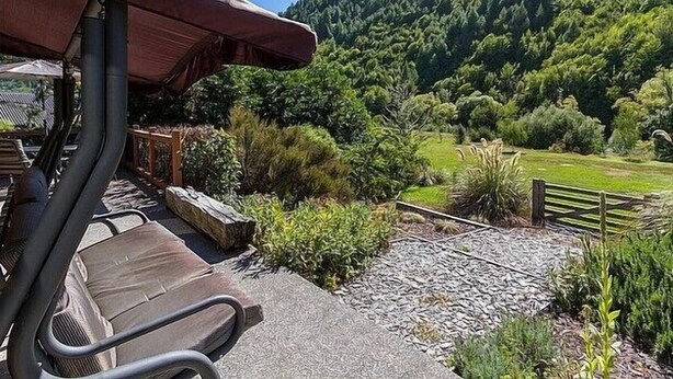 Een terras met buitenmeubilair, uitzicht op een bebost glooiend landschap en een grindpad naar een houten hek.