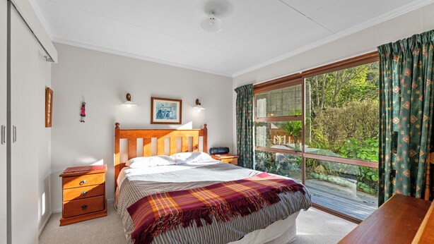 A bedroom with a bed, bedside tables, a window with curtains, and a view of greenery outside. - Ruatotara - Pukawa Holiday Home (Pukawa Bay)
