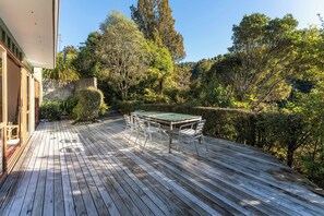 A wooden deck with a table and chairs, surrounded by dense greenery and trees.