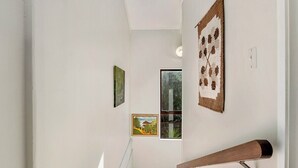 A staircase with a wooden handrail, white walls, and three framed artworks. - Ruatotara - Pukawa Holiday Home (Pukawa Bay)