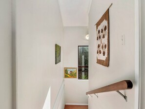 A staircase with a wooden handrail, white walls, and three framed artworks.