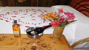 A bed with a white sheet, a decorative pillow, a bottle, a spoon, and a vase with flowers. - Intillama Jungle Lodge (Fernando Lores)