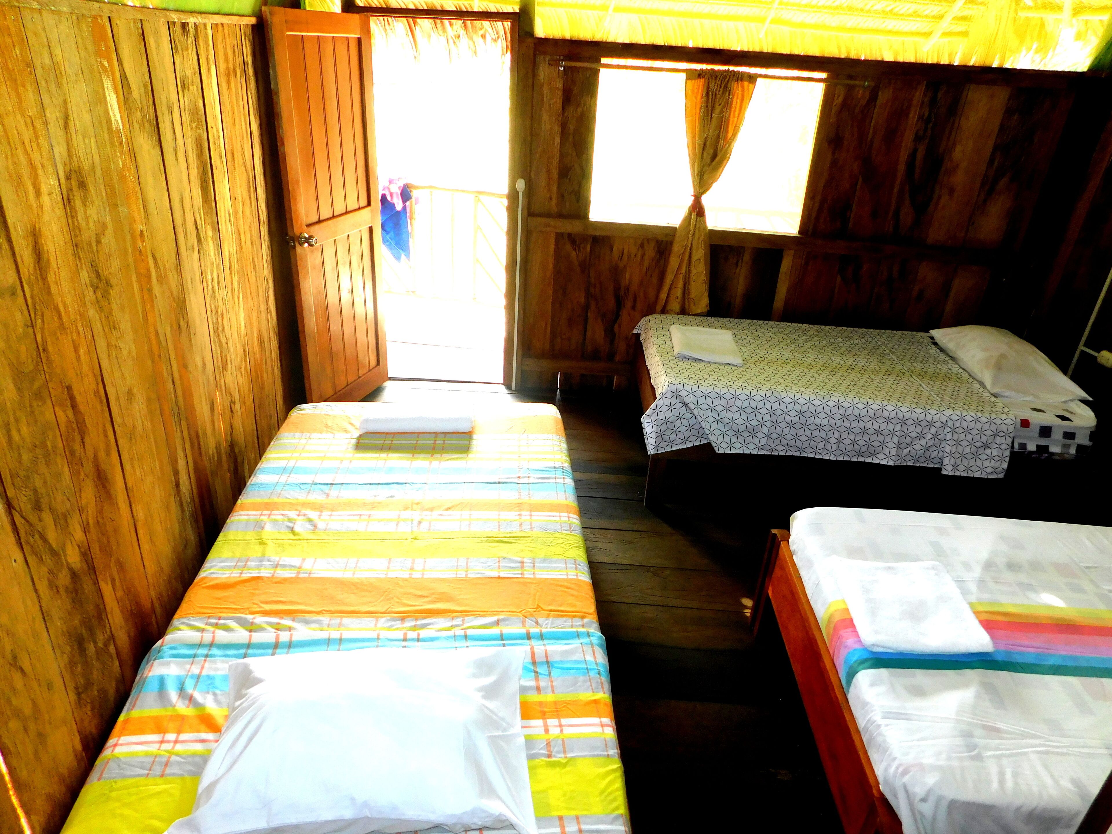 A small, rustic room with two single beds, wooden walls, and a window with curtains.