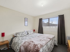 A hotel room with a large bed, a nightstand with a lamp, a window with curtains, and a framed picture on the wall. - Lakewood - Omori Holiday Home (Omori)