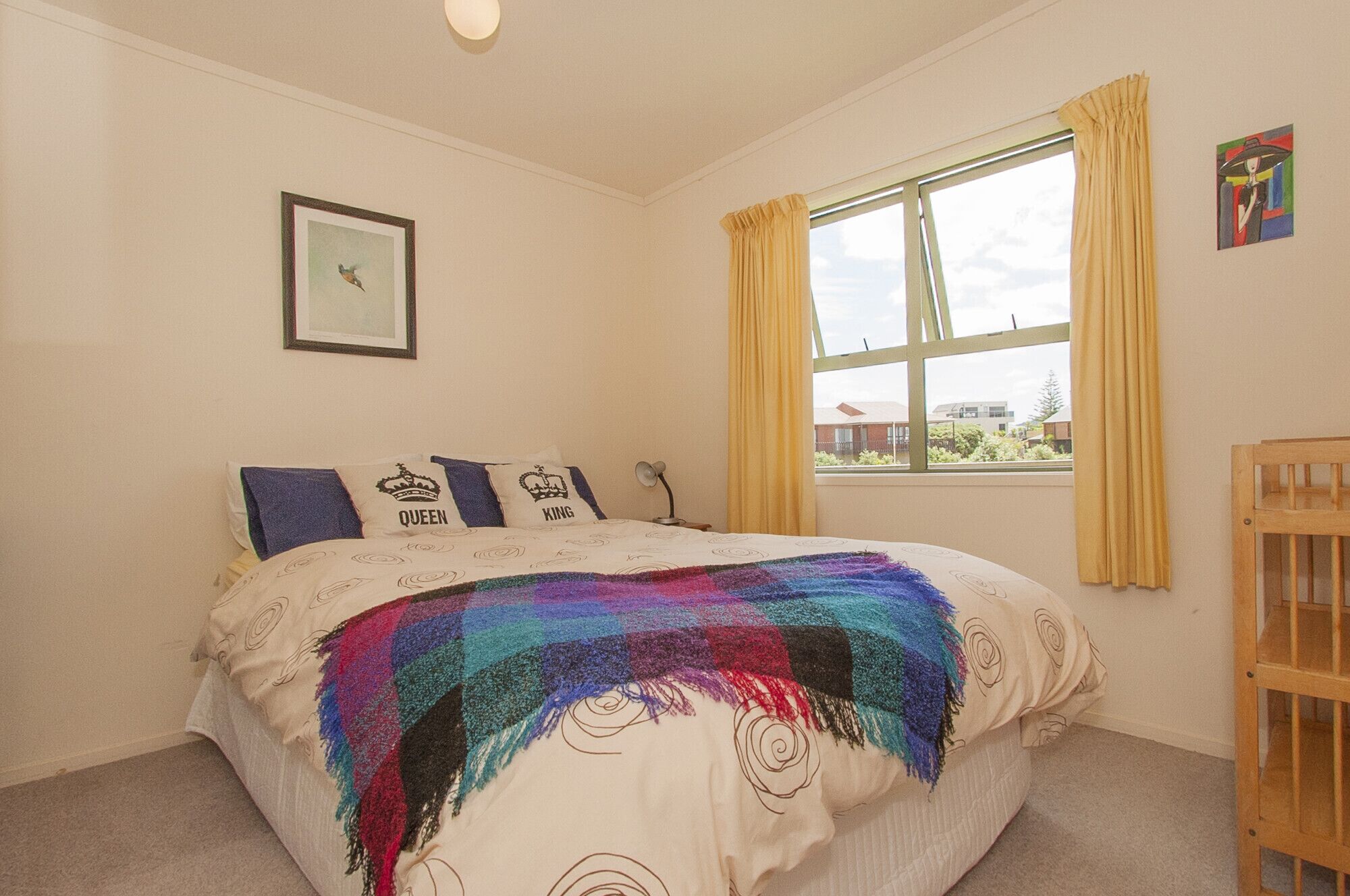 A bedroom with a bed, a window with curtains, a picture on the wall, and a small wooden cabinet.