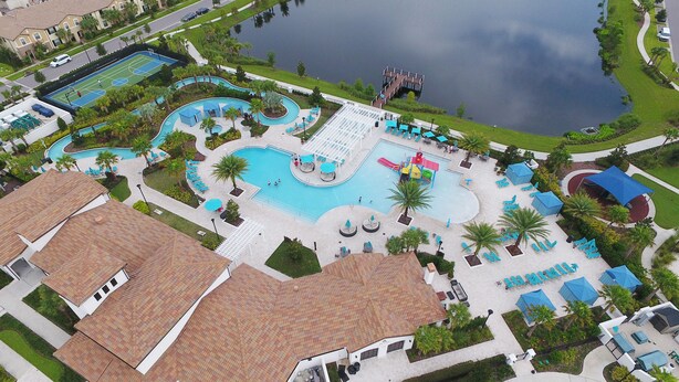 Luchtbeeld van een resort met een groot centraal zwembad, meerdere kleinere zwembaden en een tennisbaan.