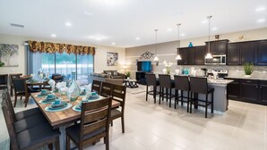 Een moderne keuken met donkere kastjes, een centraal eiland en een eethoek met een houten tafel en stoelen.