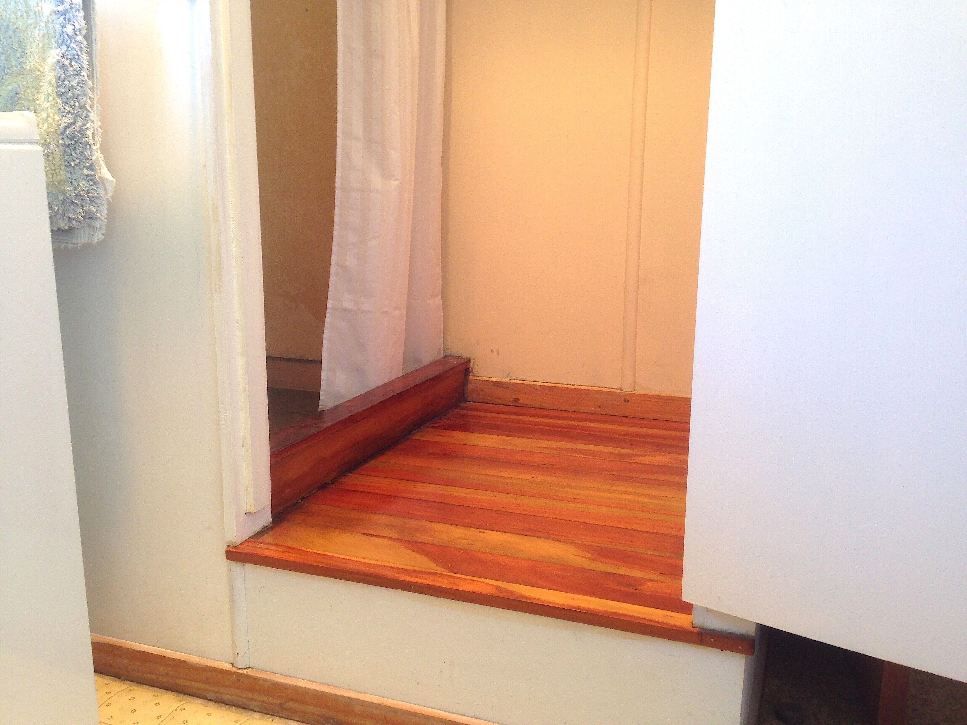 A small, narrow room with wooden flooring and a white wall.