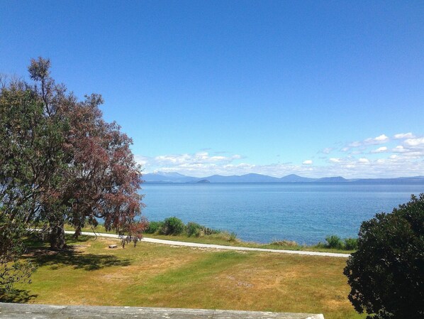 A clear view of a lake with mountains in the distance, a grassy area with trees, and a paved path along the water's edge. - Relax Lakeside - Five Mile Bay Holiday Home (Five Mile Bay)