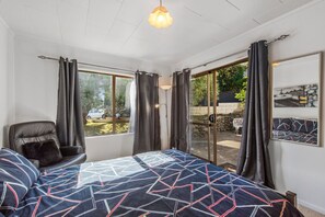 Quarto com uma cama grande, uma cadeira e vista para o exterior por uma porta de correr de vidro.