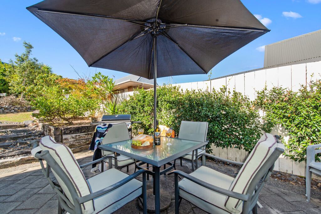 Une terrasse extérieure avec une table en verre, quatre chaises et un grand parasol.