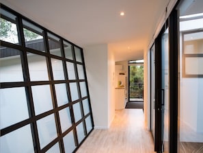 Un couloir moderne avec une cloison en verre, un espace cuisine et une vue sur l’extérieur.