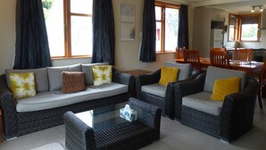 A living room with a sofa set, a coffee table, and a dining area with chairs and a table. - Snowed Inn - Ohakune (Miro) Holiday Home (Ohakune)