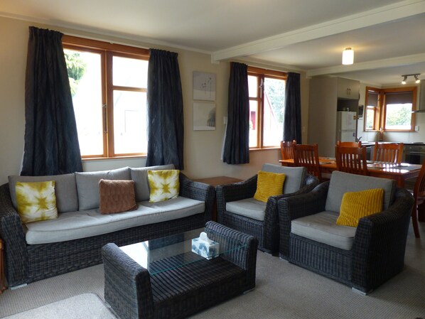 A living room with a sofa set, a coffee table, and a dining area with chairs and a table. - Snowed Inn - Ohakune Miro Holiday Home (Ohakune)