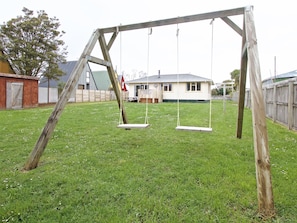 A wooden swing set in a backyard with a house in the background.