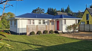 A two-story house with a red door, a fenced front yard, and a clear blue sky. - Snowed Inn - Ohakune (Miro) Holiday Home (Ohakune)