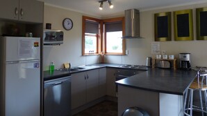 A modern kitchen with stainless steel appliances, a built-in oven, and a large window providing natural light. - Snowed Inn - Ohakune (Miro) Holiday Home (Ohakune)