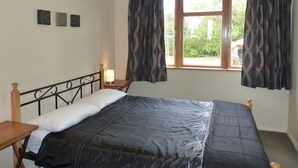 A single bed with a headboard, a bedside table, and a lamp. There is a window with curtains and a view of greenery outside. - Snowed Inn - Ohakune (Miro) Holiday Home (Ohakune)