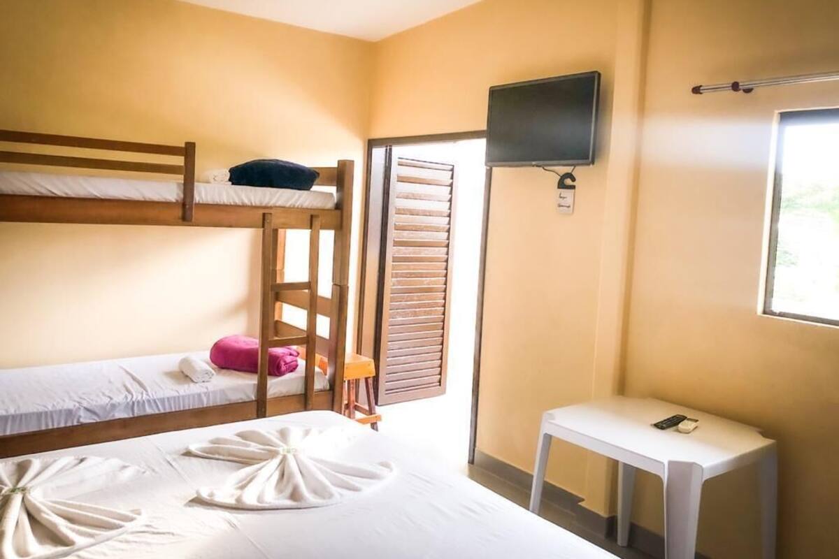 A room with bunk beds, a TV mounted on the wall, a small table, and a window with blinds.