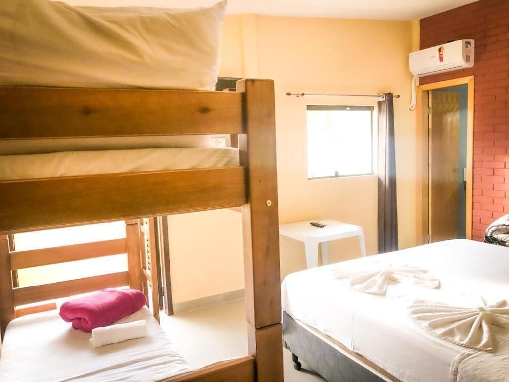 Un lit superposé avec une serviette rose et du linge de lit blanc, un lit simple avec du linge de lit et des serviettes blancs, une petite table blanche et une fenêtre avec vue.