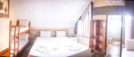 Habitación de hotel con literas, una cama individual, cabecero de madera, una ventana y una puerta que da a un baño.