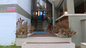 Entrada de un edificio moderno con un cartel que indica la dirección a la entrada y un recordatorio de lavar los pies.