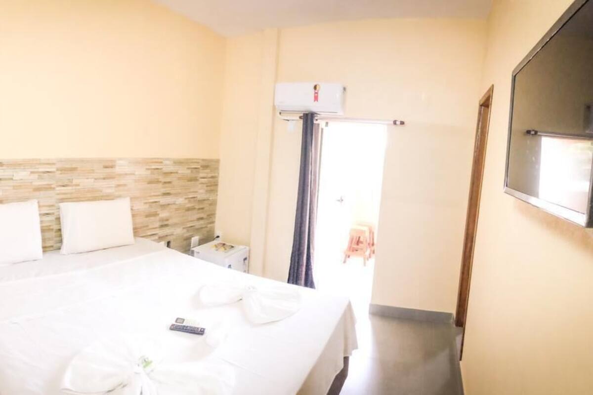 A hotel room with a bed, a bedside table, a wall-mounted TV, and a window with a curtain.