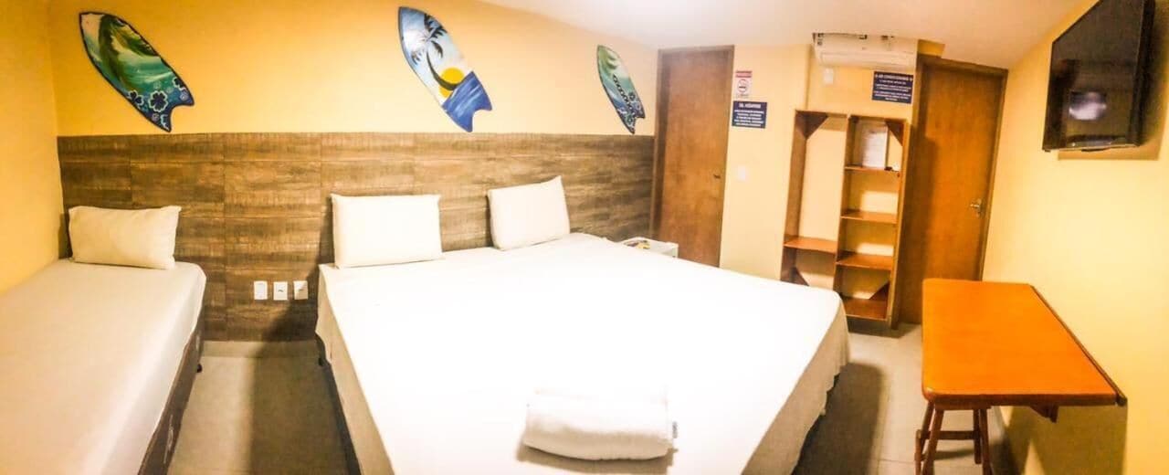 Une chambre d’hôtel avec un grand lit, deux lits simples, une tête de lit en bois, une petite table et des œuvres d’art accrochées aux murs.