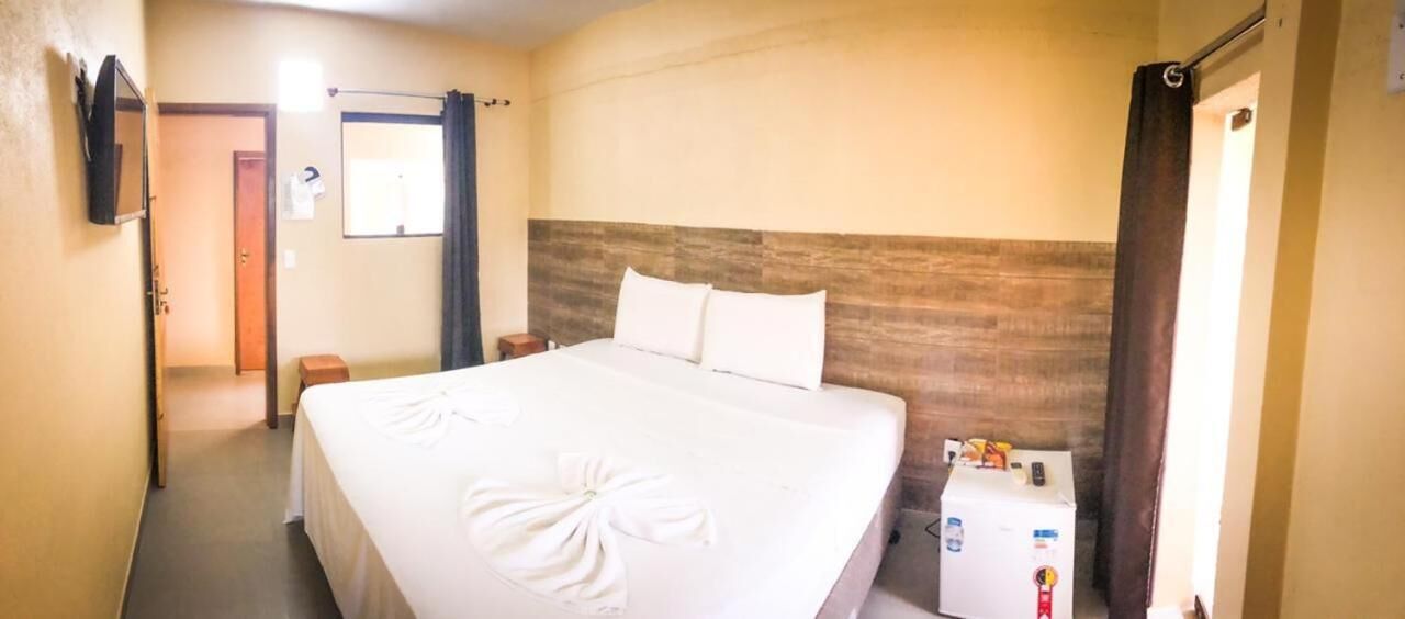 A hotel room with a large bed, a wooden headboard, a bedside table, and a small cabinet.