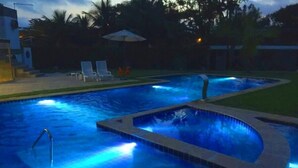 Una piscina con una cascada pequeña y algunas sillas reclinables al fondo.