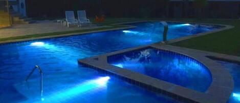 A swimming pool with a small waterfall feature and a few lounge chairs in the background.