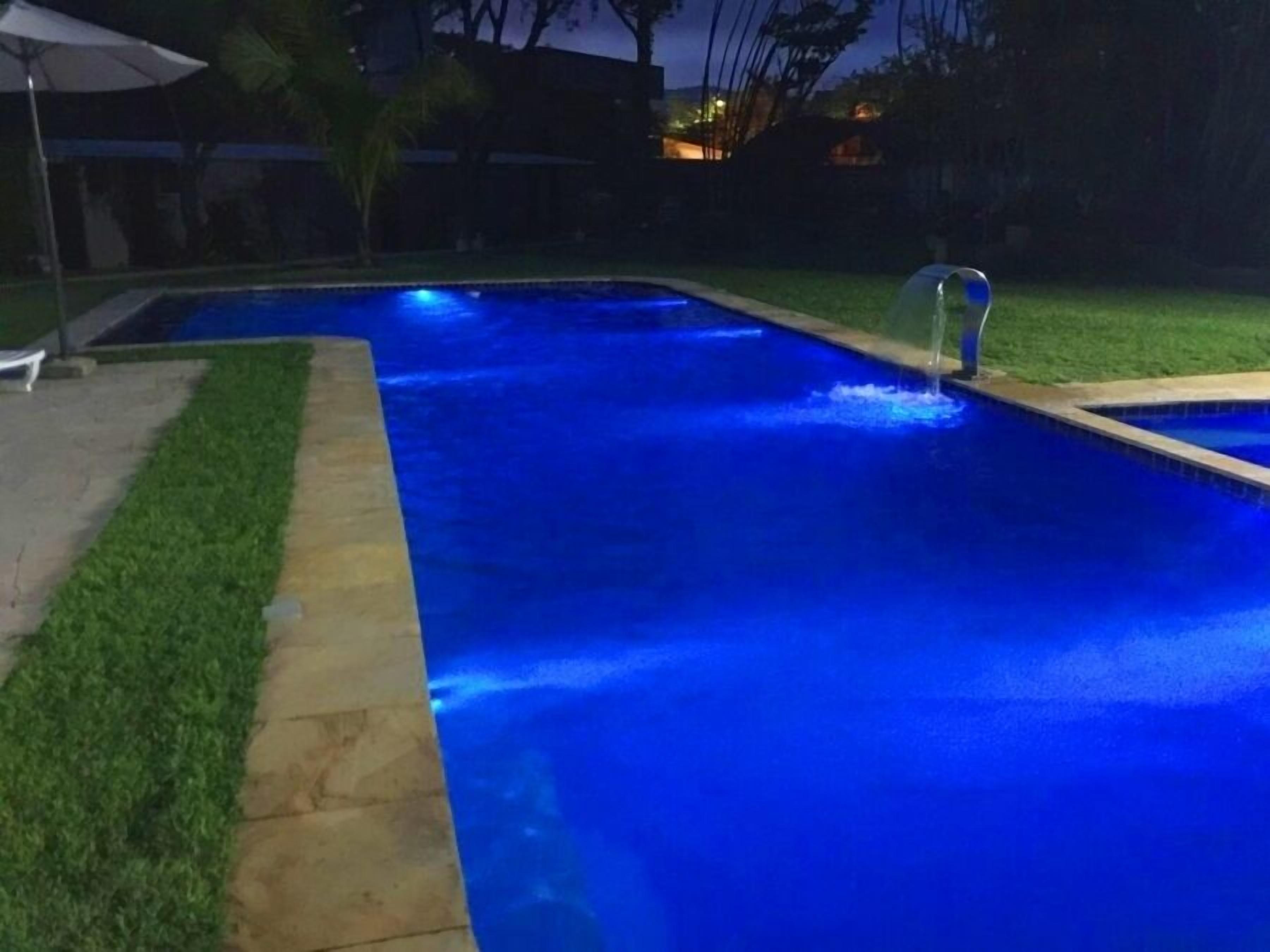 A rectangular swimming pool with a water feature at one end, surrounded by a well-maintained lawn and a stone border.