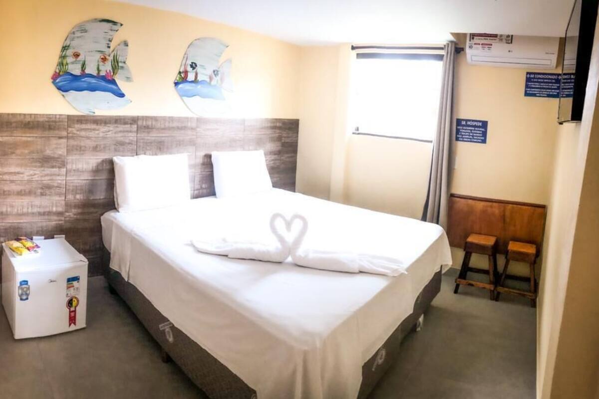 A hotel room with a bed, a small table with toiletries, and a wall with artwork.
