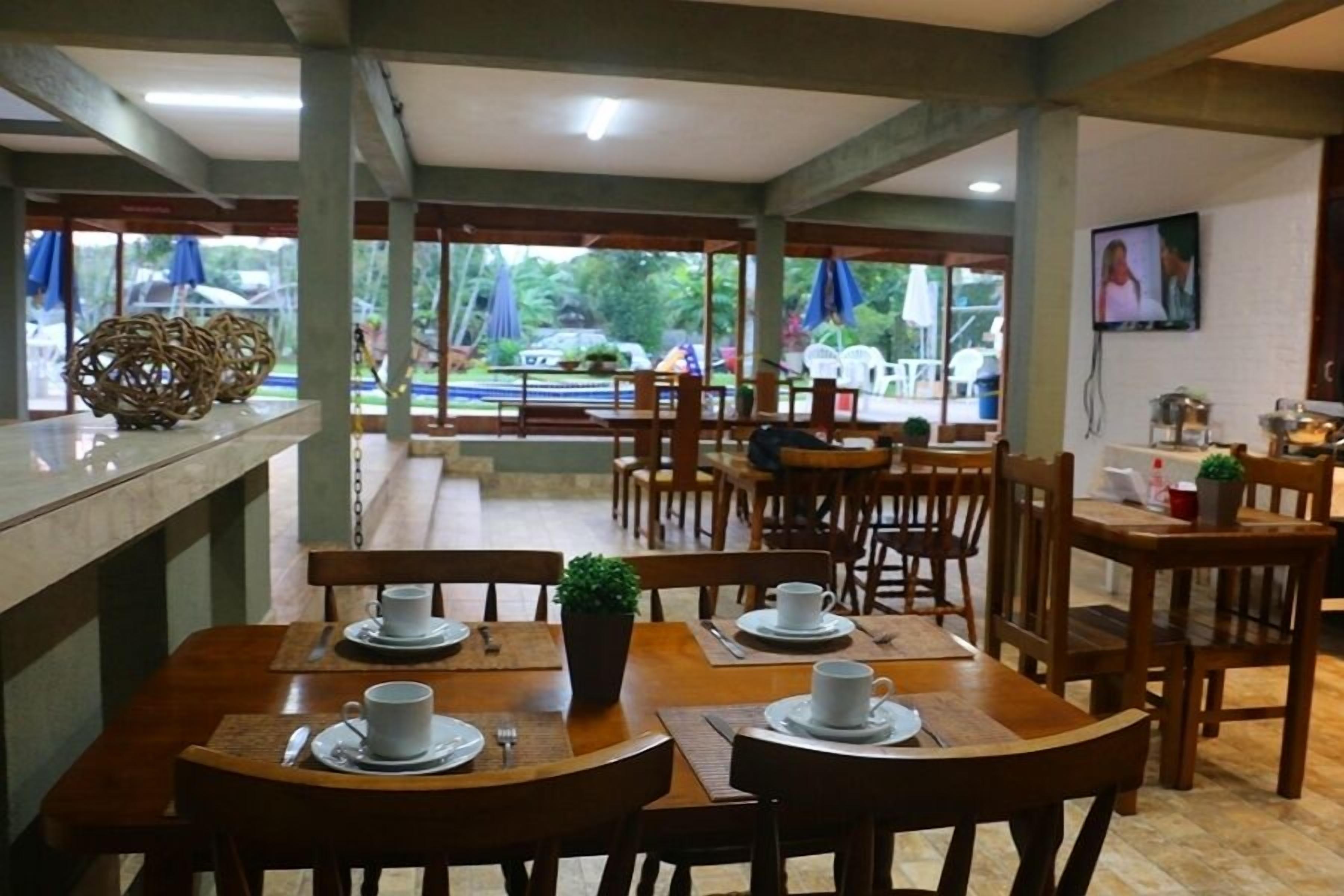 A restaurant with wooden tables and chairs, white cups and saucers, and a TV on the wall.