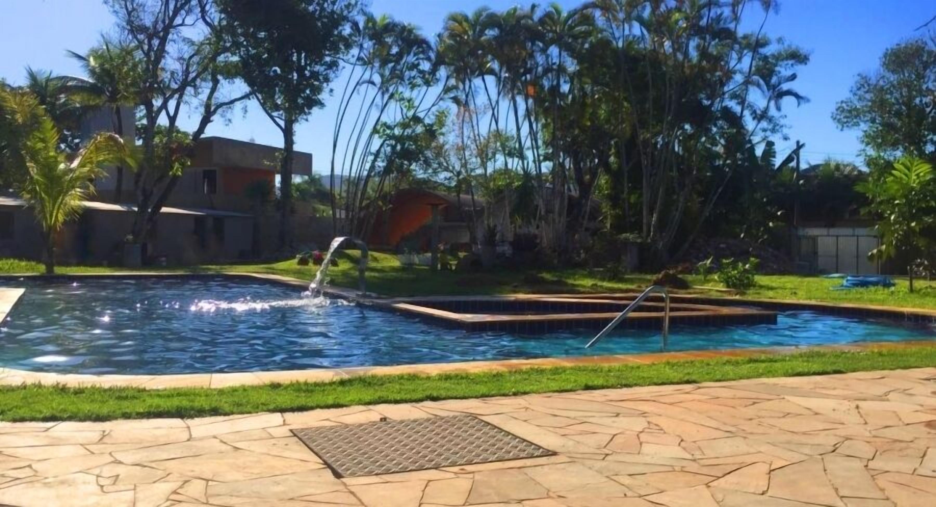 Una piscina con caída de agua, rodeada de palmeras y un camino pavimentado.