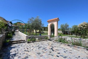 Un patio con un camino de piedra, un pequeño arco y un jardín con plantas y una hamaca.
