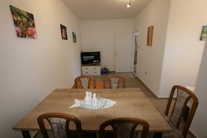 Un comedor con una mesa de madera, cuatro sillas y un televisor al fondo.