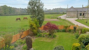 A rural landscape with a fenced field, a stone building, and a variety of vegetation.