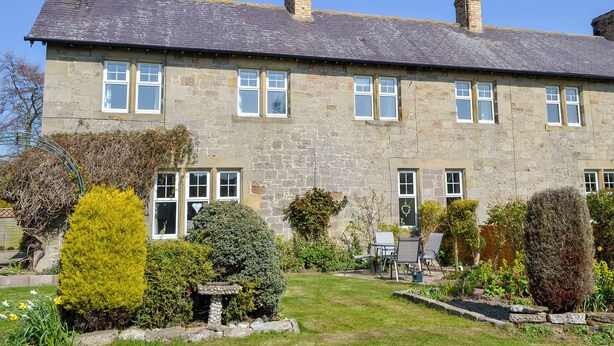 A stone house with multiple chimneys, a garden with various plants, and outdoor seating.