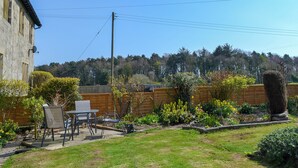 A backyard with a patio, outdoor furniture, a wooden fence, and a garden with various plants and flowers.
