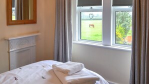 A bedroom with a bed, a window with curtains, a mirror, and a fireplace.