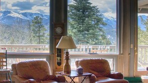 A cozy room with two leather armchairs, a wooden table, and a lamp. A large window offers a view of mountains and trees. - Eagles Rest:Mountain views>Huge home>Hiking (#23-ZONE3439) (Estes Park)